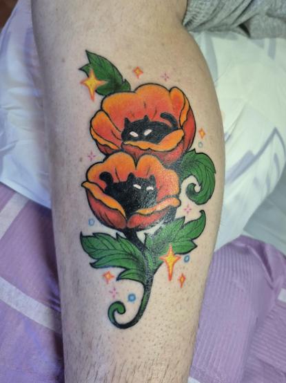Photo of a freshly coloured tattoo of some little black void cats snuggling up in some poppies as the middle of the flowers, with sparkles around them.