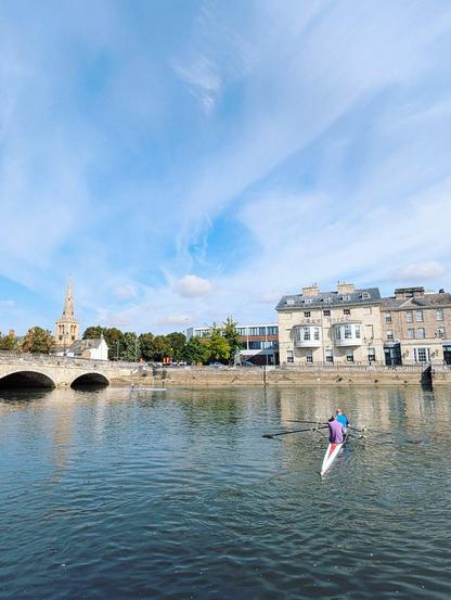 A kayak on a river, part of a bridge visible on the left and a hotel on the opposite bank