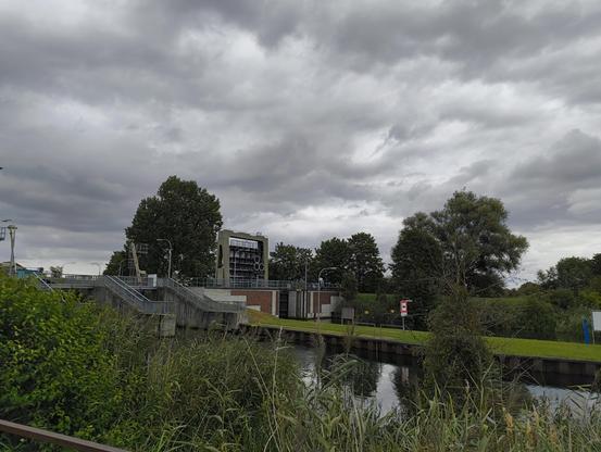 Ankunft an der Schleuse Lewitz. Hier verläuft die Elde-Müritz-Wasserstraße. Das Gewässer ist an der Schleuse zweigeteilt. Vorne ein Bereich, an welchem ein Wehr zur Regulierung des Wasserstands ist und hinten Schleuse für kleinere Boote. Eines der Schleusentore ist gerade oben. Auf einem Schild steht 'Zum Schleusen blauen Hebel ziehen'.