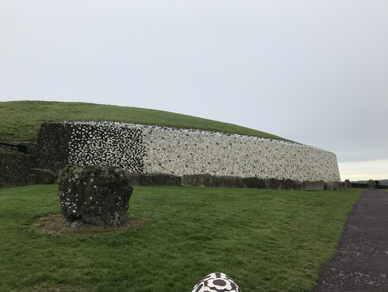 Colour view of Newgrange long white wall with a short standing stone in front of it.
