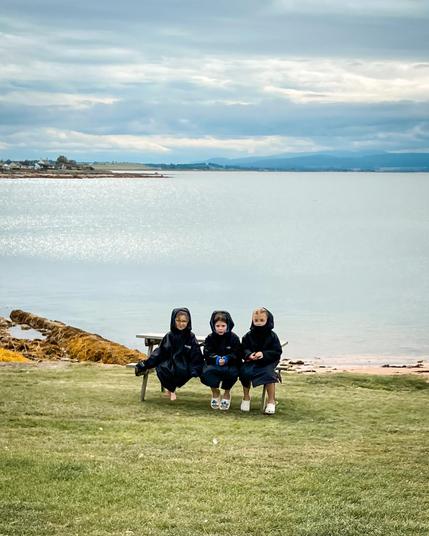 Made me laugh. 3 children sitting on a bench wearing their black ‘Dryrobes’ after swimming in the sea with their mothers at Portmahomack.