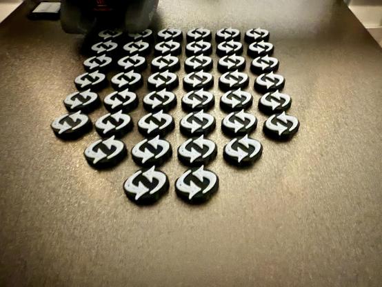 A 3D printer bed. Shows a bunch of Anno 1800 trade tokens (black with a white top)