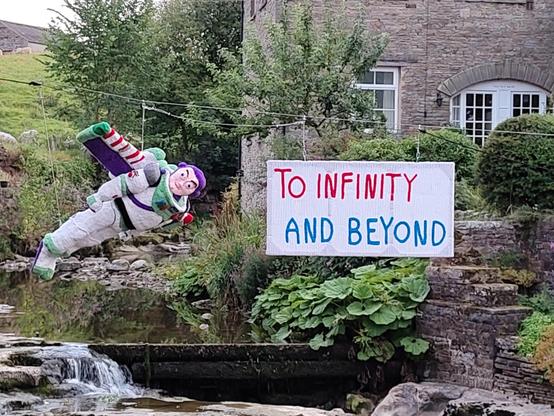Ein menschengroßer Buzz Lightyear fliegt über einen Bach, daneben ein Schild: "To Infinity and beyond"