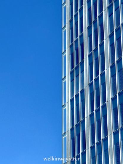 A modern glass skyscraper with vertical lines of windows, sharply divided against a clear blue sky.

ガラス張りの高層ビルが縦に並ぶ窓を見せ、澄み切った青空と鋭く対比している。