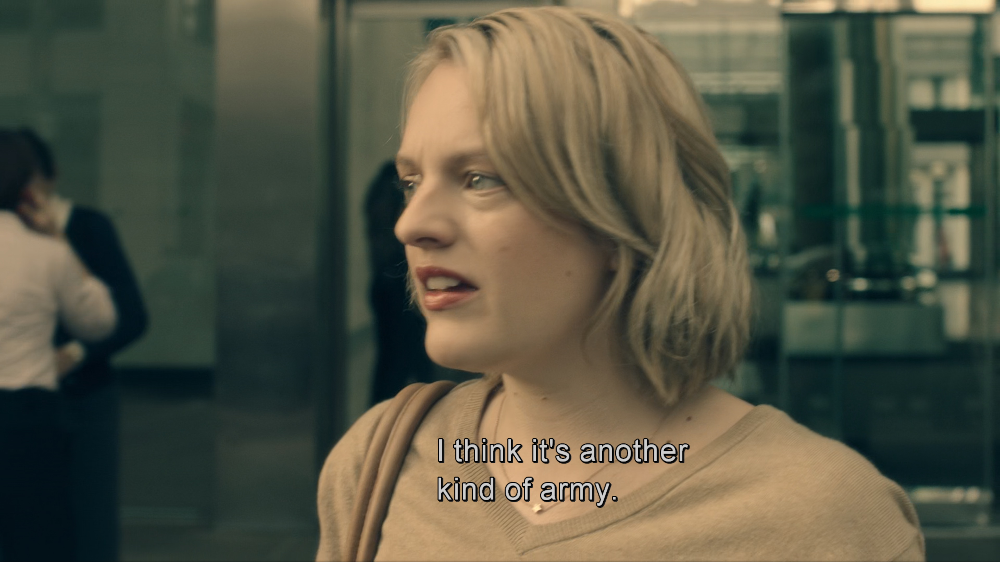 Screenshot from The Handmaid's Tale TV series. Close-up of June's concerned face as she processes both losing her job and seeing these armed forces, her blonde hair framing her worried expression. She's leaving the office building. Her subtitle reads "I think it's another kind of army" as she realizes these aren't regular military but the enforcement arm of the emerging Gilead regime.