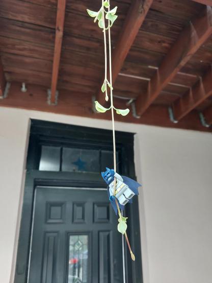 A Lego Batman climbs up a vine trailing down from a deck one storey above.