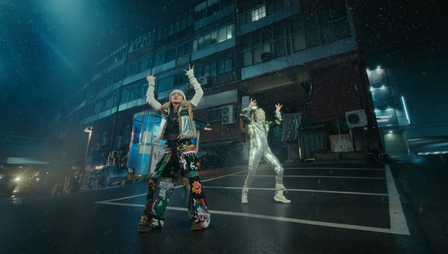 Chung Ha and a silver-clad dancer in a parking lot (?) at night.
