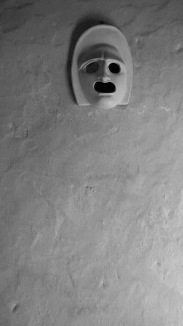 Earthen mask on a wall, with the tormented expression of someone screaming. (Version françæ) Masque en terre sur æn mur, avec l’expression tourmentæ de quelqu’æn qui crie.