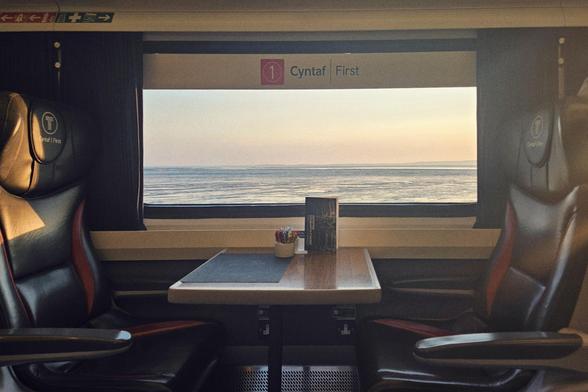 View of the coast and sea through the picture window of the 1st class carriage. Two dark brown leather chairs facing wache other, brown table in-between.