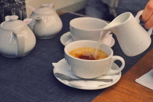 Someone is pouring milk in the cup of tea. All white porcelain.