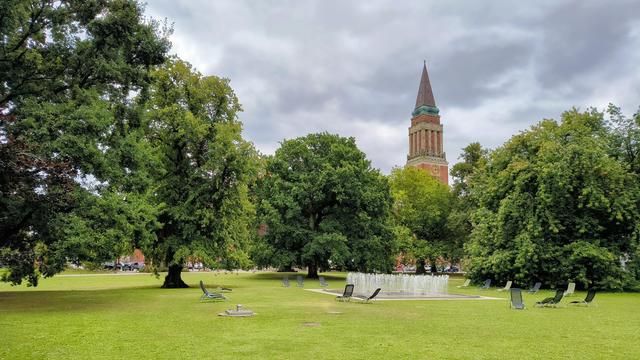Springbrunnen und Liegestühle im Hiroshimapark in Kiel, dahinter der Rathausturm vor wolkenverhangenem Himmel