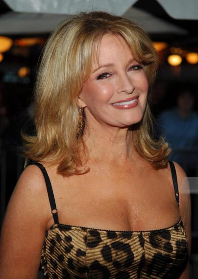 Deidre Hall at the 2005 Daytime Emmy Awards wearing a sleeveless leopard print dress with thin black straps. Her blonde hair is styled in soft waves, and she accessorizes with earrings. The dimly lit background suggests an event setting. Her confident pose and bold fashion choice exude glamour and attitude, making a statement on the red carpet.