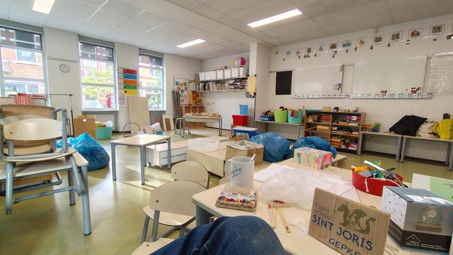 Een klaslokaal met kasten, bakken, tafels en stoelen een beetje kriskras door het lokaal nog