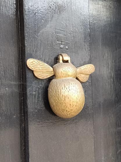 An einer schwarzen tür ist ein Türklopfer angebracht, der die Form einer Biene mit Flügel hat