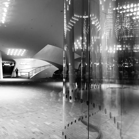 black and white photograph of a lone figure guarding a staircase. complex reflections in curved glass surface are visible in one half of the frame