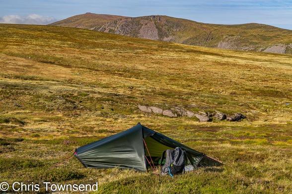 A small green tent pitched on a grassy slope in the hills glowing gold in the early morning sun..