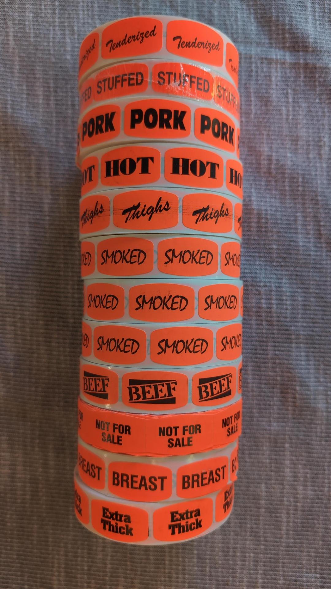 A stack of rolls of deli stickers, including such bangers as: Tenderized, stuffed, pork, hot, thighs, smoked, smoked, smoked, beef, not for sale, breast, and extra thick.