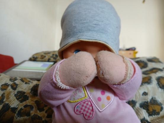 an old doll with a grey hat and pink clothes holding her hands in front of her eyes