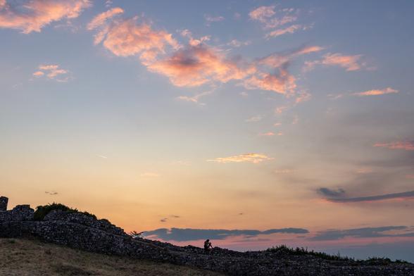 A person sitting on ancient stone walls at sunset, with pink clouds scattered across the sky.
