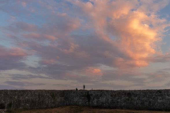 Silhouettes of people standing on top of a historic stone wall beneath a colorful sunset sky.