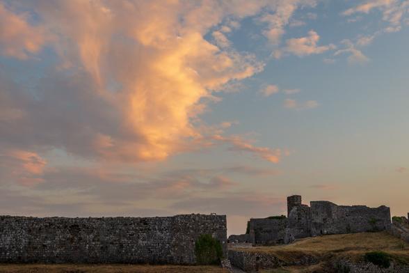 Stone fortress walls and ruins under a golden cloud formation during sunset.