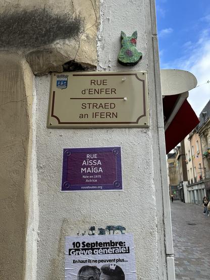 Sous la plaque de rue (rue d’enfer) à Redon, écrit aussi en breton. Une affiche au format d’une plaque de rue avec le nom : Rue Aïssa Maïga actrice née en 1975 et en plus petit Noustoutes.org. 
En dessous une affiche coupé pour une grève générale le 10 septembre.