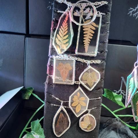 English Closeup on a store window full of jewelry: necklaces made of stained glass and real pressed plants and insects wings.
Français Gros plan sur une vitrine de magasin pleine de bijoux : colliers en vitrail et avec de vraies plantes et ailes d'insectes pressées.