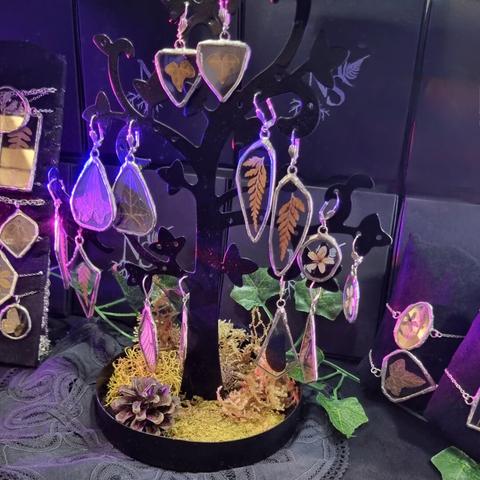 English Closeup on a store window full of jewelry: earrings made of stained glass and real pressed plants and insects wings.
Français Gros plan sur une vitrine de magasin pleine de bijoux : boucles d'oreilles en vitrail et avec de vraies plantes et ailes d'insectes pressées.