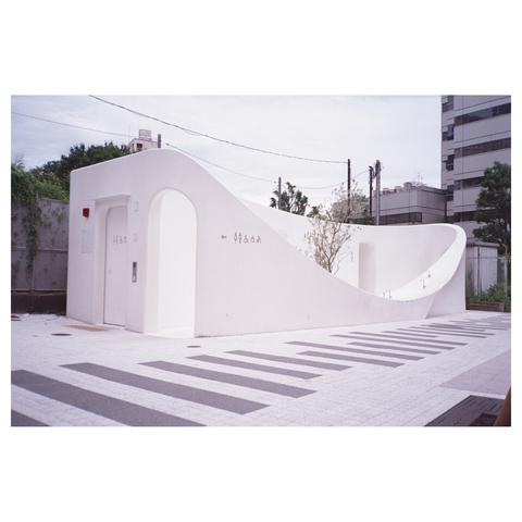 A white building with a curved outer wall that reaches almost to the ground in the middle. A tree stands in the "forecourt" behind it.