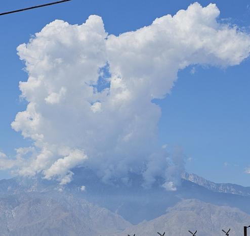 Mountain San Jacinto with white clouds rising from its summit like smoke against a clear blue sky