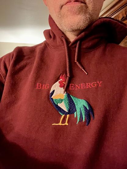 Close up selfie of me in a maroon hoodie. Embroidered on the front is the word "big" and then an embroidered rooster, and then the word "energy". I'm really into chickens.