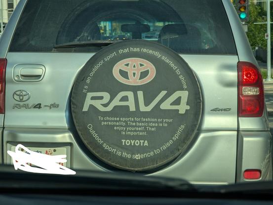 A photo of the back of a Toyota RAV 4, with a cover over the spare tire.

The cover features a slightly off-centre Toyota logo and the RAV4 wordmark but with weirdly soft edges.

Underneath those is some text that reads:

"To choose sports for fashion or your
personality. The basic idea is to
enjoy yourself. That
is important.

TOYOTA"

Additionally, written along the top and bottom edges of the circular cover:

"It s an outdoor sport  that has recently started to shine."

"Outdoor sport is the sicence to raise spirits."

The spelling, spacing and punctuation is transcribed as seen. Except that the owner has attempted to correct the spelling of "science" with white paint or correction fluid.