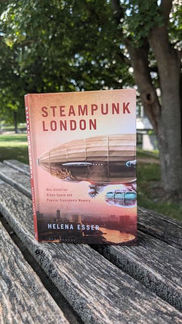 Helen Esser's book "Steampunk London" on a wooden bench in a park setting
