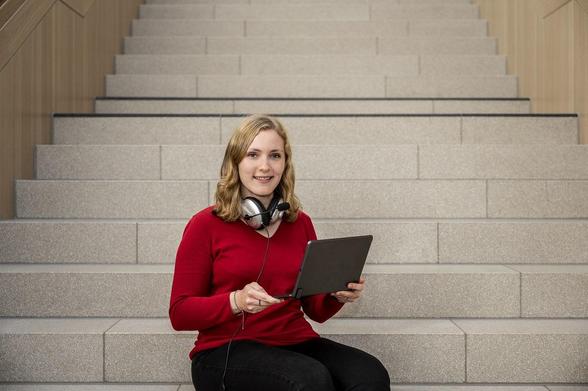 Studienberaterin auf einer Treppe mit Laptop und Kopfhörern für virtuelle Beratungen.