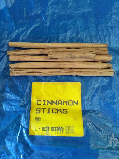 A blue bag with a handful of cinnamon sticks on top.  A yellow sticker reads 'Cinnamon Sticks' and has a best before date of 1996