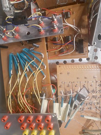 Many handbuilt electronic circuit boards together in a box, components, wires (some cut), nanana connectors and aluminum front panels are visible.