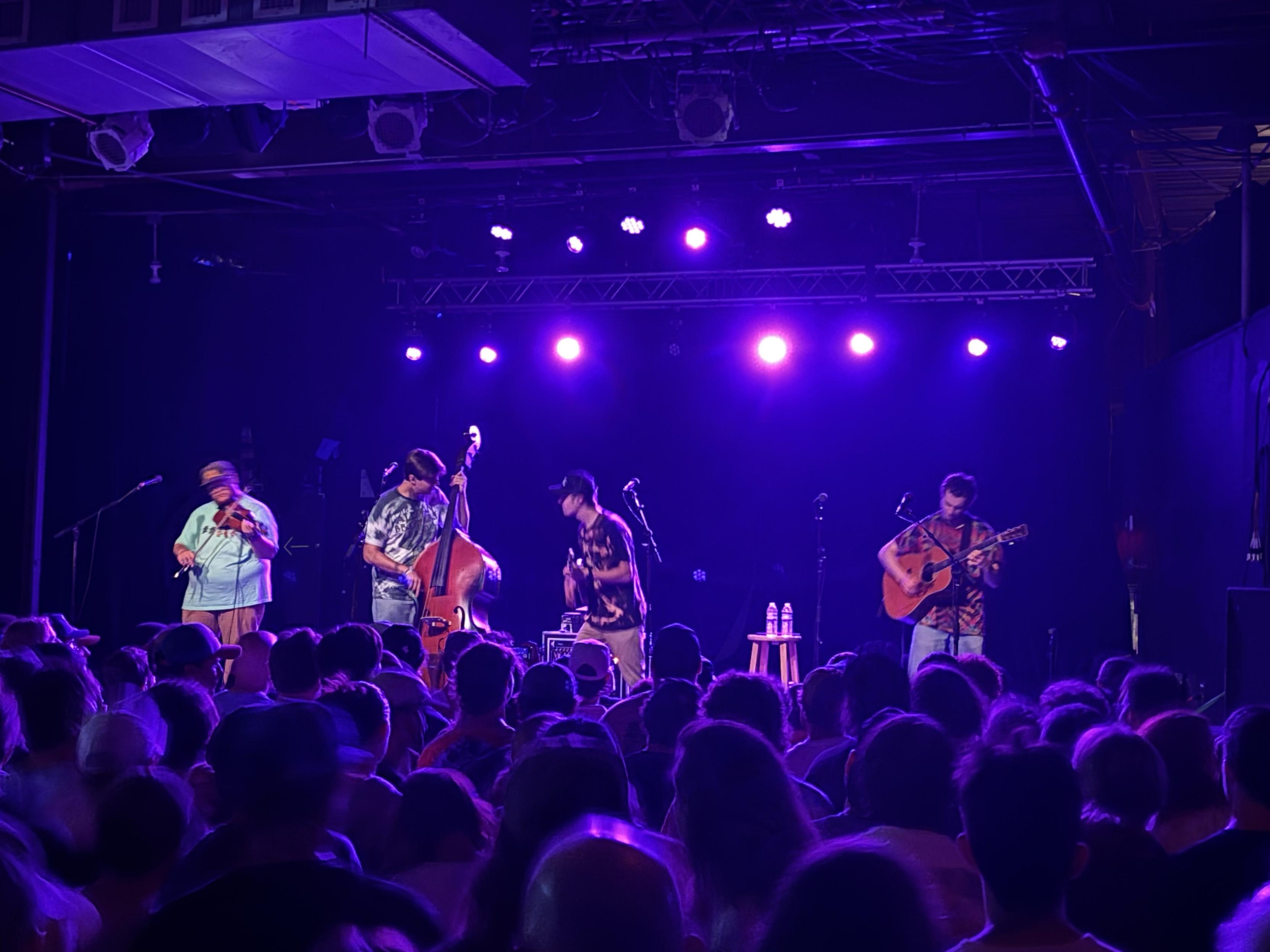 Guitar, mandolin, bass and fiddle on stage in a small crowded club.
