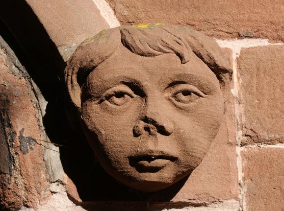 A carving in red sandstone of a young man's face, perhaps a novice monk, with a placid expression.