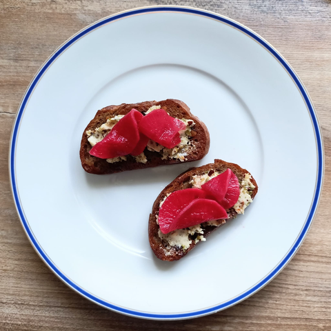 Auf einem Teller zwei geröstete Brotscheiben mit der KApernbutter und etwas Pinke Rettich