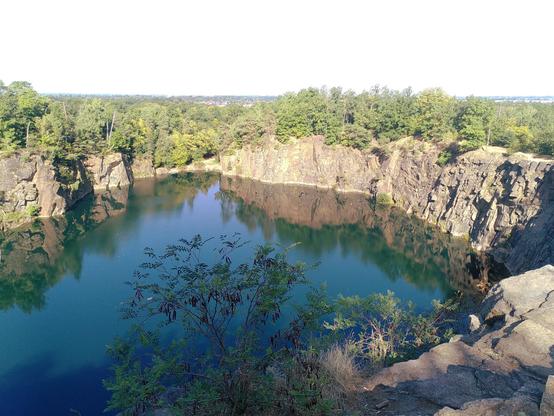 An old quarry, fringed with trees and water filled. View from the top, the sun in the back.