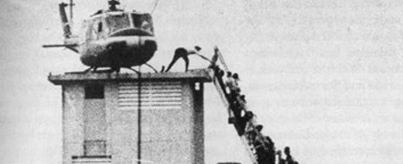 a chopper on a roof, and a person reaching for a line of people coming up some stairs - this is a photo of the last chopper out of Saigon