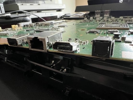The removed motherboard of a PlaySation 4 with the HDMI port bent at a nasty angle, with many of the internal pins pulled off of the center post as well.
