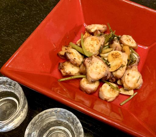 Sliced octopus sautéed with paprika, served in a red square bowl.
