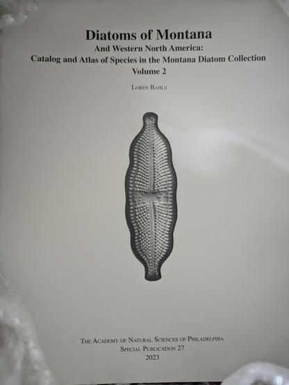 Crummy photo of the book in the box it shipped in, because it's too heavy to lift out easily. It features an image of a diatom that looks like a leaf, banana, or pea pod, I dunno.

The cover reads: 

Diatoms of Montana And Western North America: Catalog and Atlas of Species in the Montana Diatom Collection

Volume 2

LOREN BAHLS

THE ACADEMY OF NATURAL SCIENCES OF PHILADELPHIA
SPECIAL PUBLICATION 27
2023