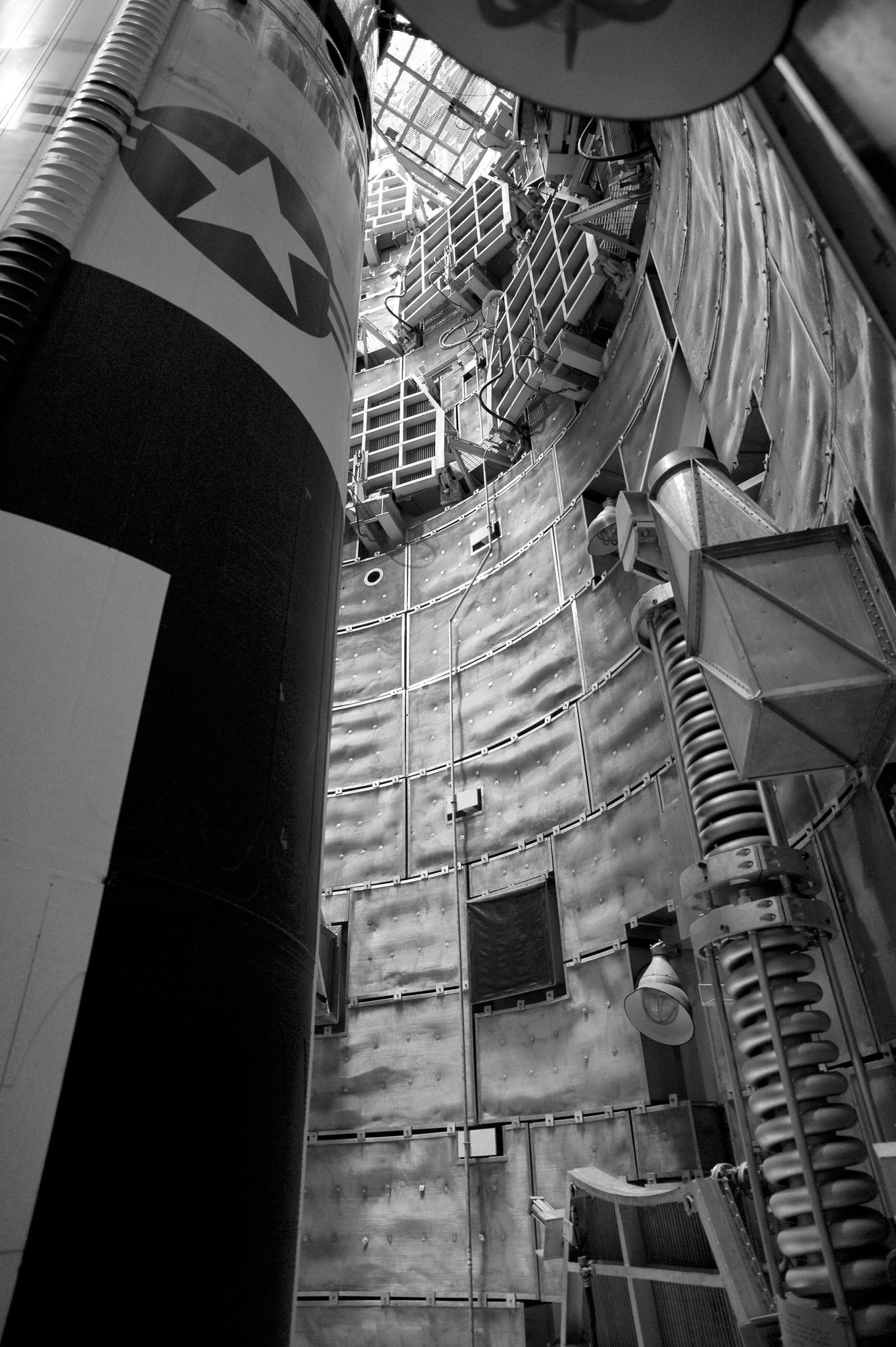 A missile pointed up inside a cramped underground silo, which is lined with retractable platforms and various apparatus.
