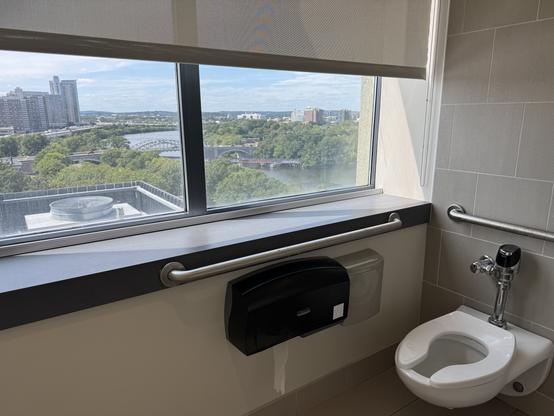 A stunning view through a wall-to-wall window of the BU Bridge and the bend in the Charles on a brilliant summer day. In the foreground is a toilet.