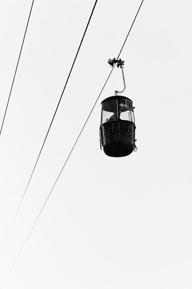 Black and white photograph of a gondola suspended on one of three visible steel cables.