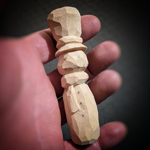 A hand holding an unpainted, carved, wooden, snowman ornament.