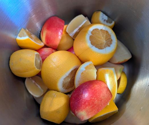 Mehrere Zitronen, Äpfel und Orangen liegen angeschnitten oder geviertelt in einem Edelstahlbehälter.