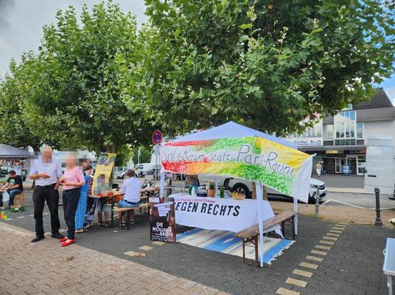 Ein Pavillon mit einem bunten Transparent: Soli-Raum statt Parkraum. Einige umstehende Menschen. Kinder, die an Biertischen malen.